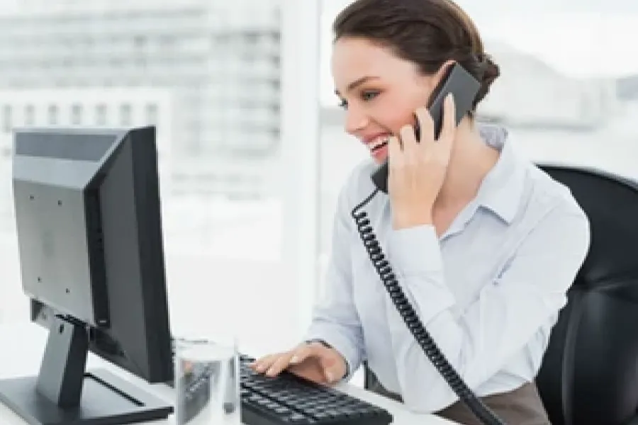 woman sitting at desk, talking on phone, and working on computer