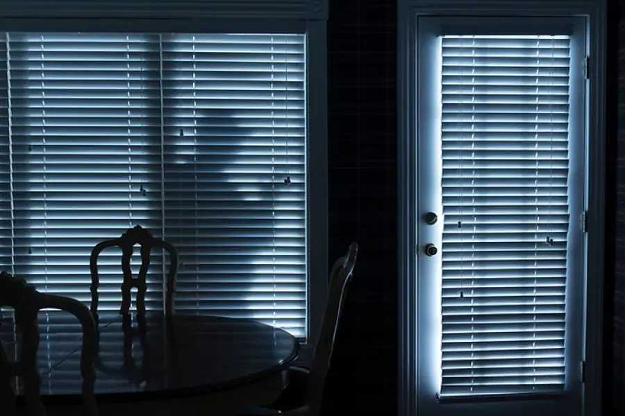 inside of dark house, with shadow of burglar outside seen through the window blinds