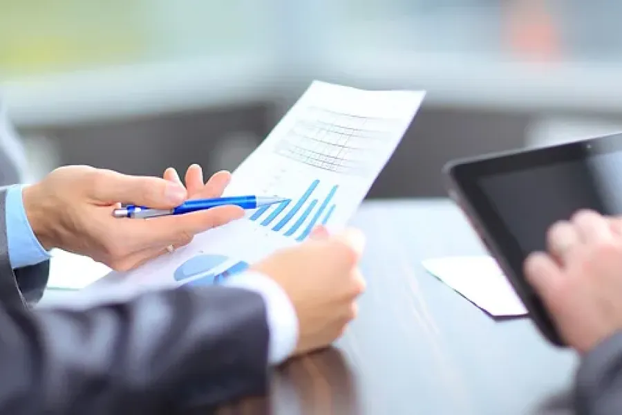 close up of hands holding a paper with graphs and another person holding a tablet