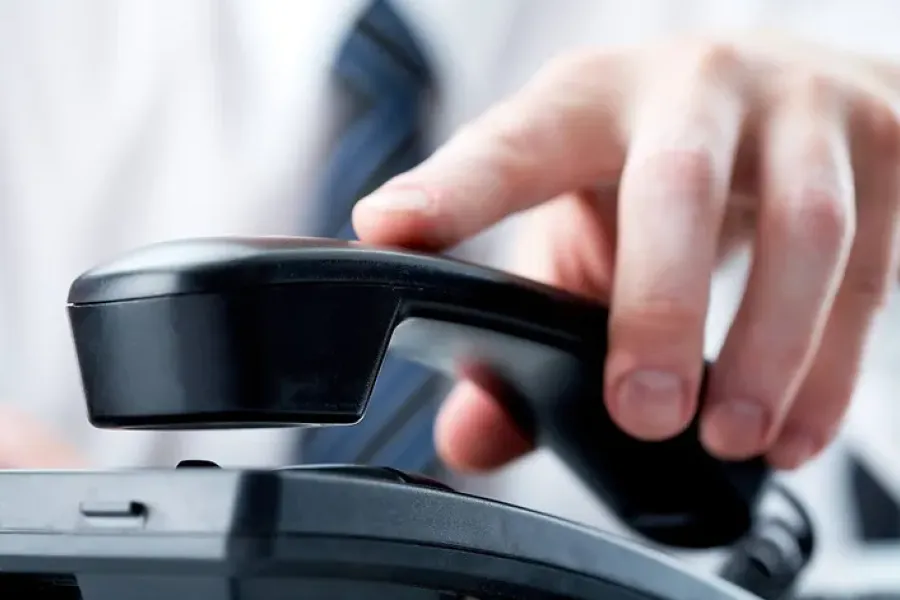 close up of hand picking up office phone on desk