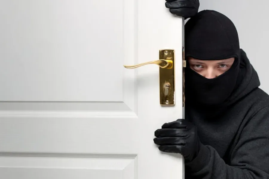 man wearing balck and ski mask peering at camera from behind door