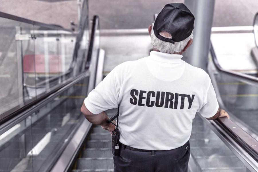 security guard in white shirt going down escalator, back of shirt reads "security""