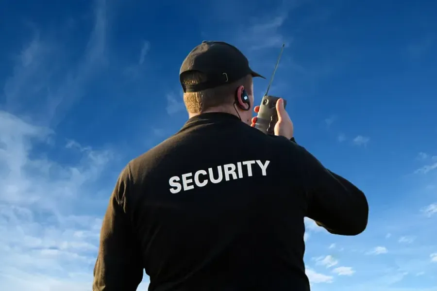 view of back of security officer talking into radio, set against bright blue sky