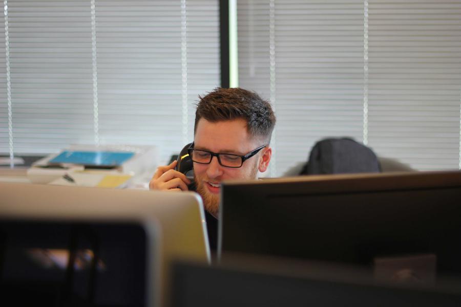 man answering phone while sitting behind two computer screens