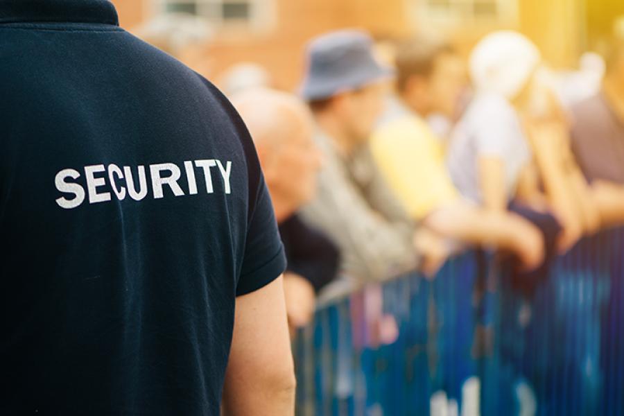 close up of back of security guard shirt standing outside at event, shirt says "security" on back