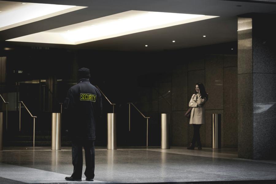 security officer in foreground outside city building with woman on phone in background