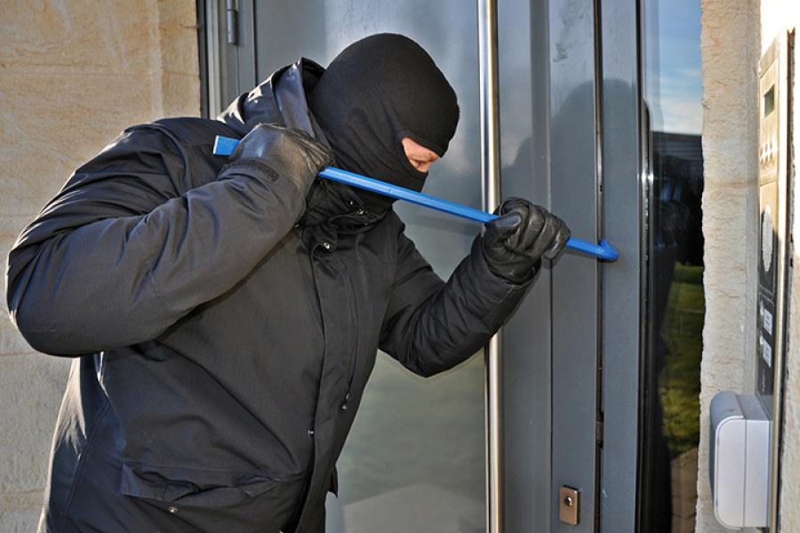 man wearing black clothes and mask using crowbar to break into building