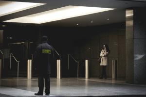 security officer in foreground outside city building with woman on phone in background