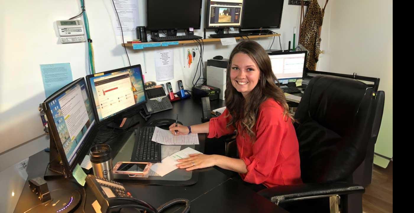 female dispatcher looking toward camera sitting at desk with two monitors