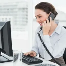 woman sitting at desk, talking on phone, and working on computer