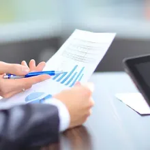 close up of hands holding a paper with graphs and another person holding a tablet