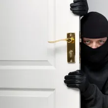 man wearing balck and ski mask peering at camera from behind door