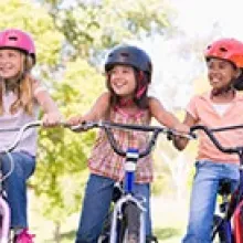 three girls riding bicycles wearing helmets