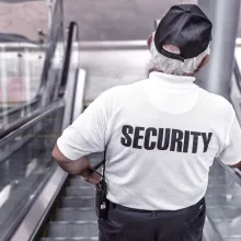 security guard in white shirt going down escalator, back of shirt reads "security""