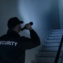male security officer in dark room shining flashlight upstairs