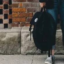 student standing on sidewalk holding backpack, only the legs are visible