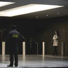 security officer in foreground outside city building with woman on phone in background