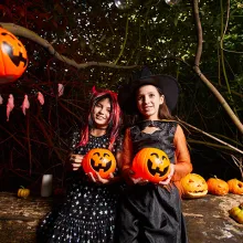 two girls dressed in costumes for halloween holding pumpkins