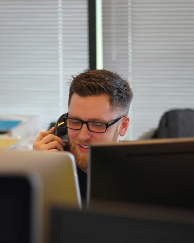 man answering phone while sitting behind two computer screens