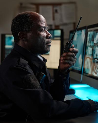 officer watching remote monitoring screens, talking on radio